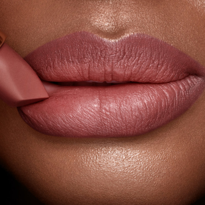 Lips closeup of a deep-tone model applying a mid-toned muted nude-rose matte lipstick.
