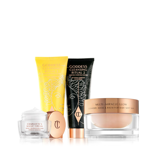 Two facial cleansers, one in lemon-yellow packaging and the other in charcoal-black, with rose-gold coloured lids, a travel-size face cream in an open glass pot with a gold-coloured lid, and a three-in-one cleansing balm in a glass jar with a gold-coloured lid.