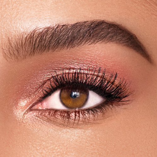 Single-eye close-up of a deep-tone model with brown eyes wearing shimmery rose gold eyeshadow.