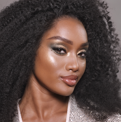 Deep skin model wearing green and gold disco 70s makeup look.