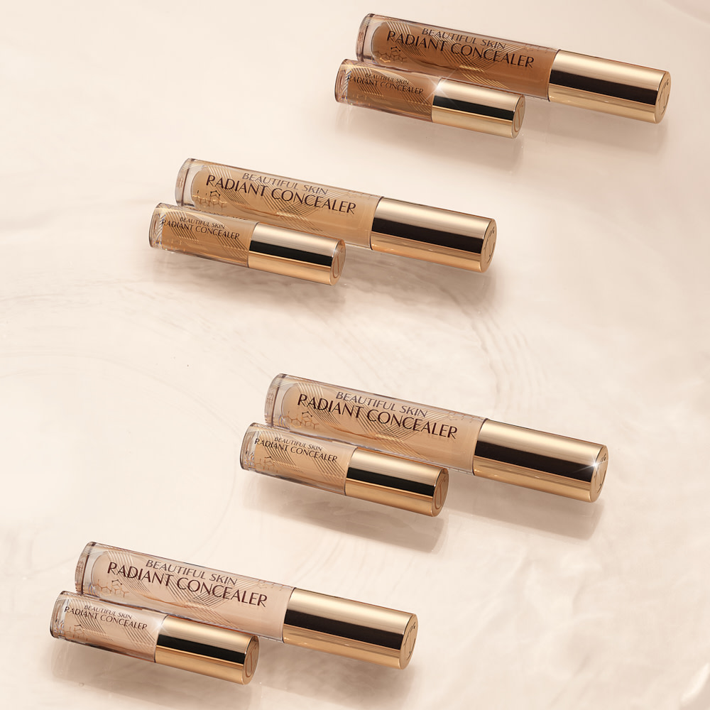 Collection of full-size and travel-size radiant concealers in a glass tubes with a gold-coloured lids with text on the tube that reads, 'Beautiful Skin Concealer'