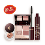 An open, mirrored-lid quad eyeshadow palette with beige, brown-gold, rose gold, and dusky pink shades, a mascara in black, and cream eyeshadow in a coppery-gold shade in a glass pot with a dark brown-coloured lid. 