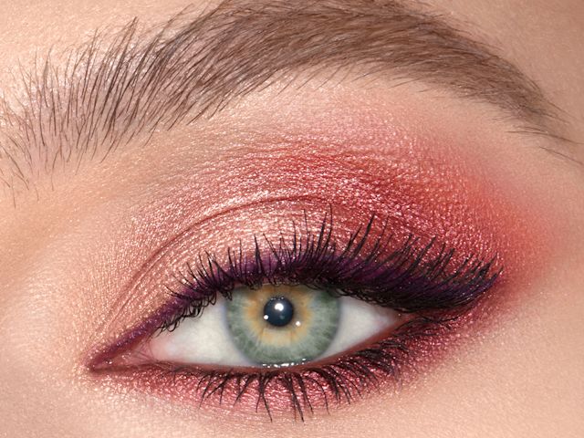 A close-up of a single green eye with shimmery maroon, copper, and gold eye makeup along with plum eyeliner. 