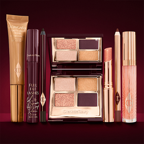 A highlighter wand in a copper-gold-coloured tube with a mascara, eyeliner pencil, quad eyeshadow palette with shimmery and matte rose gold, plum, and golden shades, an open lipstick in nude coral, lip liner pencil in nude red, and a lip gloss in nude pink. 