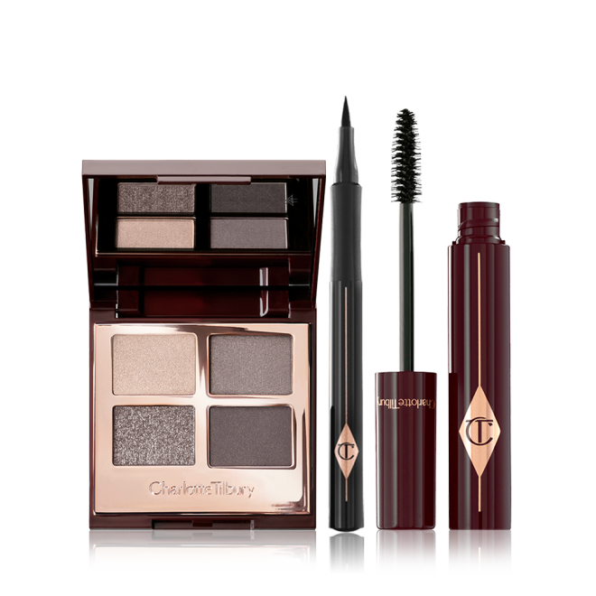 An open, quad eyeshadow palette in smokey grey shades with an open, black-coloured eyeliner pen, and an open mascara with its applicator in a dark-crimson colour scheme. 