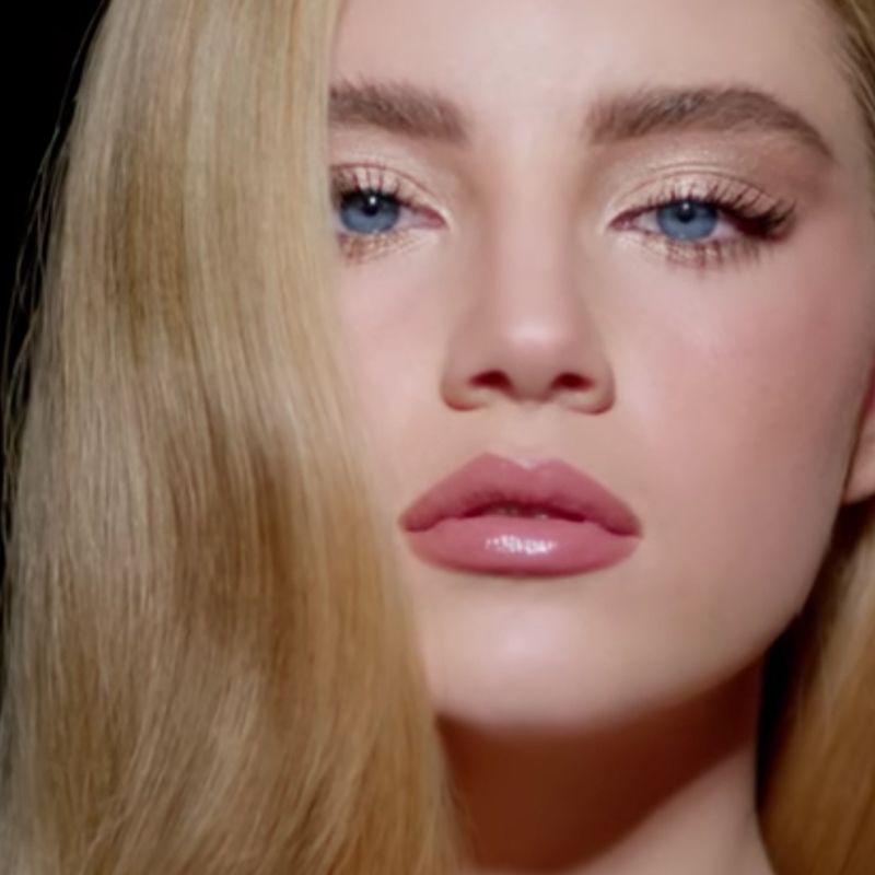 A fair-tone model with blue eyes wearing volumising, black-coloured mascara with glowy, nude pink makeup. 