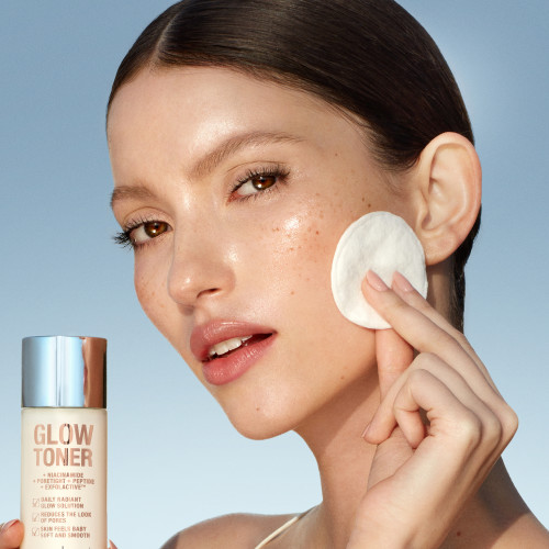 Fair-tone brunette model with glowy, luminous skin, applying glowy toner with a cotton pad.