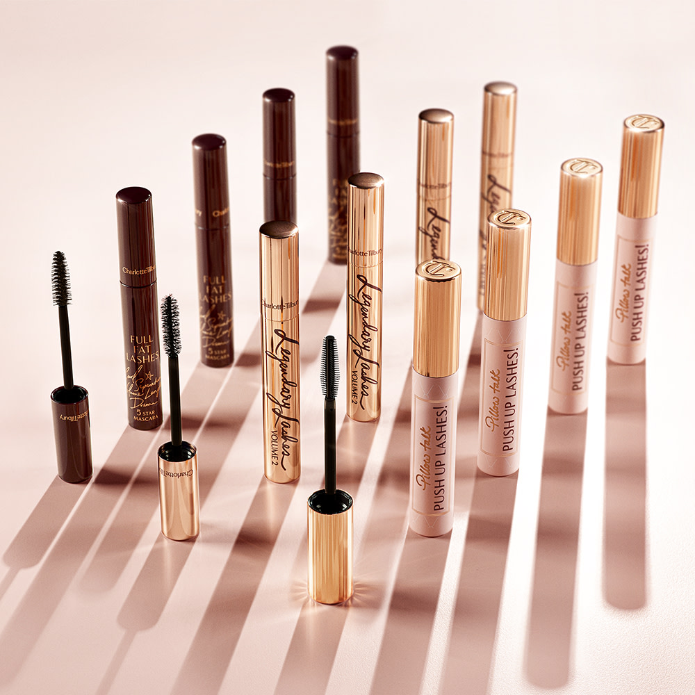 A collection of three different mascaras, one in dark crimson tube, the second in golden, and the third in a nude pink bottle with a gold-coloured lid. All three with their applicators in front of them. 