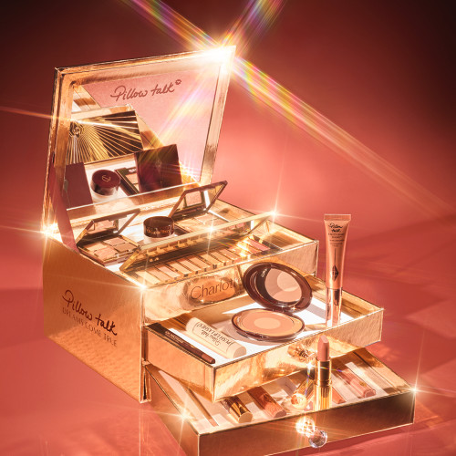 A reflective, gold-coloured chest with two drawers containing makeup items, which include Liquid highlighter wand in rose gold, black mascara, shimmery lip gloss in nude pink, glitter-free but high-shine lip gloss in nude pink, rose gold eyeshadow pigment in a petite pot, two closed lipsticks, travel-size lip gloss in nude pink, eyeliner pencil in dark brown, lip liner pencil in nude pink, quad eyeshadow palettes, 12-pan eyeshadow palette, and two-tone blush compacts.