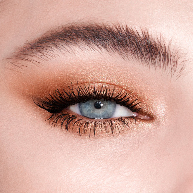 Primer plano de un solo ojo de una modelo rubia con ojos azules, maquillada con topacio brillante. 