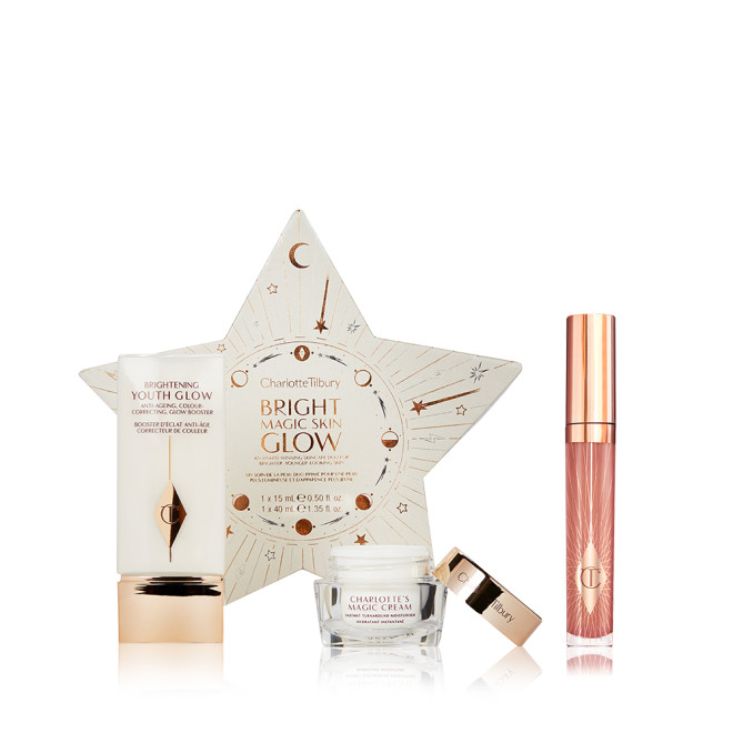 Primer in a rectangular glowy bottle with gold-coloured lid, pearly-white face cream in a glass jar with gold-coloured lid, and nude pink lip gloss along with a star-shaped, white-coloured packaging box. 