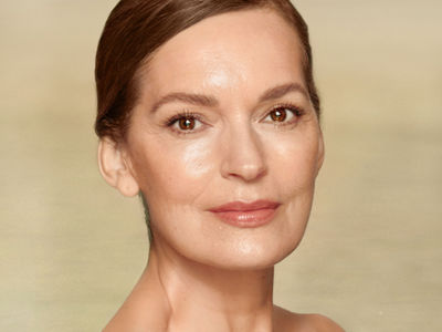 Close-up of a light-tone model with mature, glowy and flawless skin, in a pool of glimmering water with her shoulders bare. 