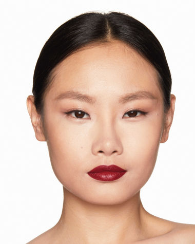 Fair-tone model with brown eyes wearing a muted wine-red lipstick with a satin finish.