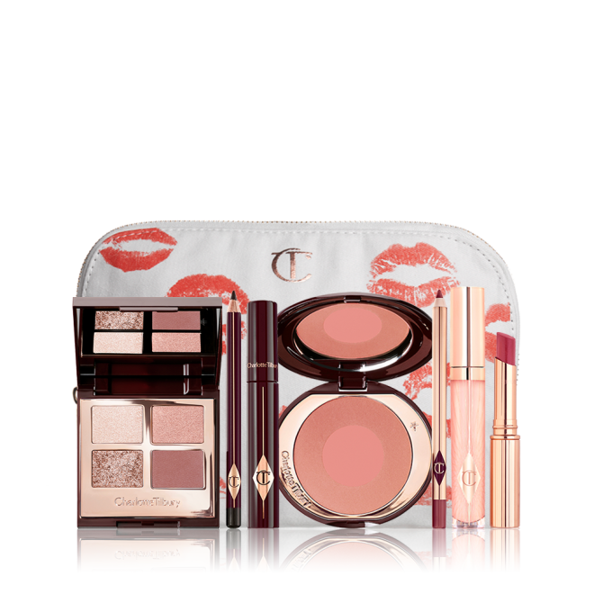 A white makeup pouch with an open two-tone blush in cool-toned brown and warm pink with a mascara, eyeliner pencil, quad eyeshadow palette with shimmery and matte brown and golden shades, an open lipstick in nude red, lip liner pencil in maroon and a lip gloss in nude pink. 