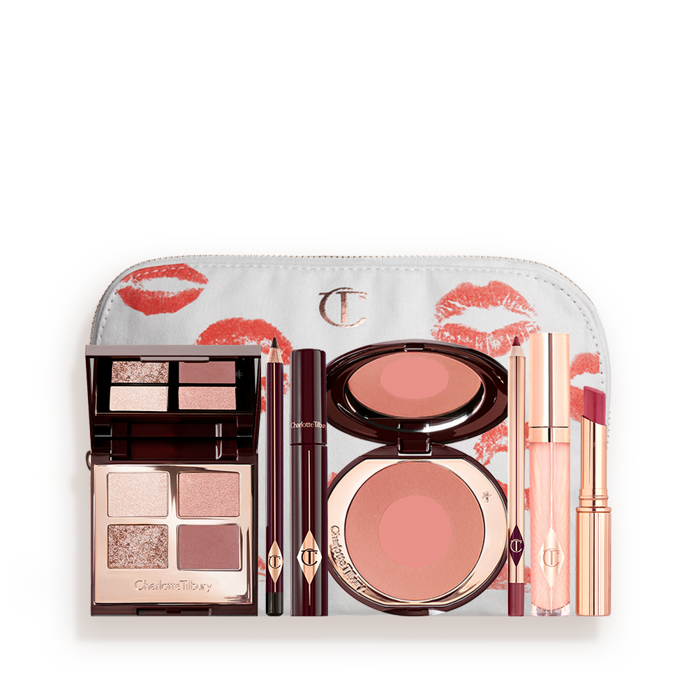 A white makeup pouch with an open two-tone blush in cool-toned brown and warm pink with a mascara, eyeliner pencil, quad eyeshadow palette with shimmery and matte brown and golden shades, an open lipstick in nude red, lip liner pencil in maroon and a lip gloss in nude pink. 