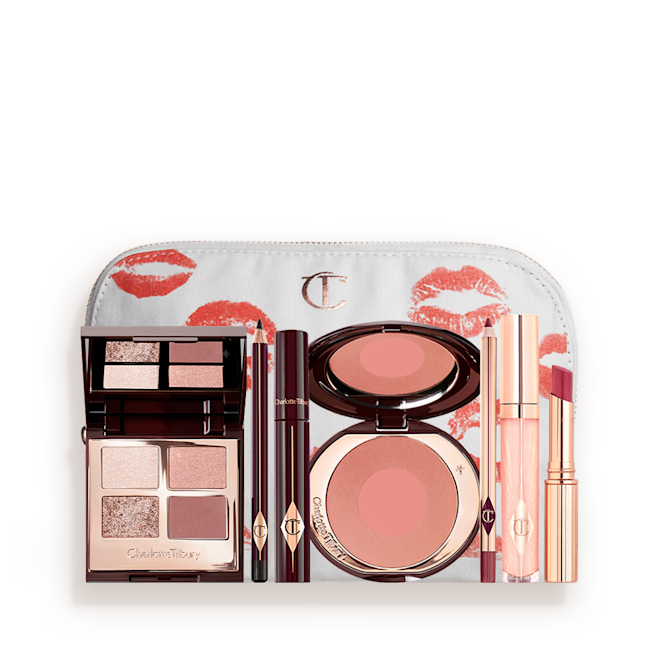 The Supermodel kit for Fair, Light and Medium tones with makeup bag displayed A white makeup pouch with an open two-tone blush in cool-toned brown and warm pink with a mascara, eyeliner pencil, quad eyeshadow palette with shimmery and matte brown and golden shades, an open lipstick in nude red, lip liner pencil in maroon and a lip gloss in nude pink.