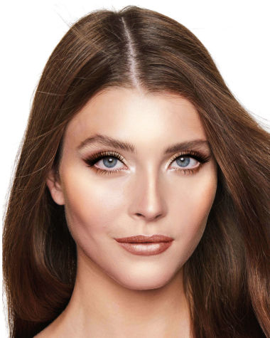 A fair-tone model with blue eyes wearing shimmery copper and gold eye makeup with black eyeliner, glowy bronzed cheeks, and pinkish-brown lipstick with gloss on top. 