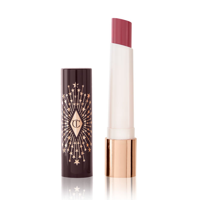 An open lipstick lip balm in a peachy nude rose shade, in white and gold tube with a black-coloured lid with gold sparkles all over it.