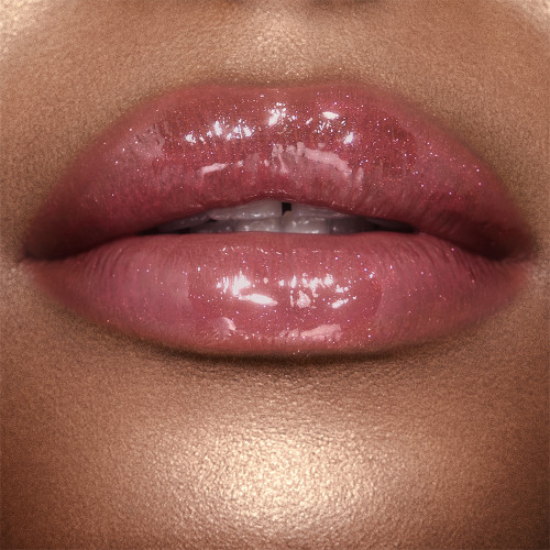 Close-up of a deep-tone model wearing a berry-pink lip gloss on her lips.