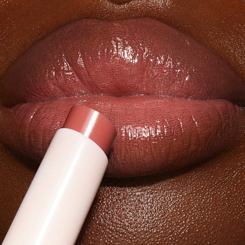 Lips close-up of a deep-tone model wearing a peachy nude rose lipstick lip balm. 