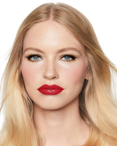 A light-tone model with blue eyes wearing shimmery bronze eye makeup with muted pink blush and glossy scarlet-red lips