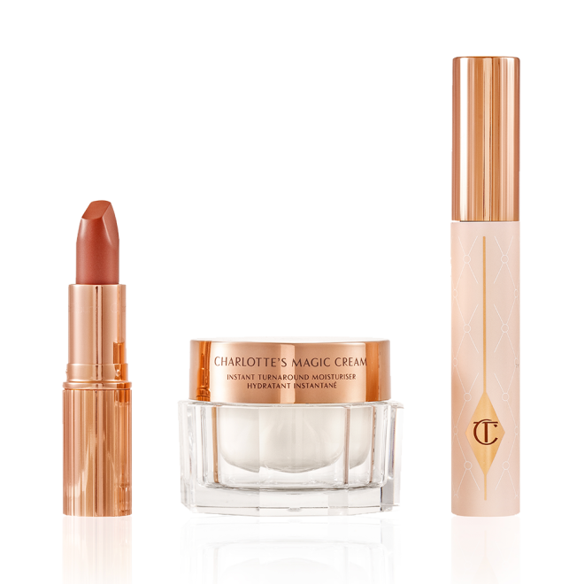 Pearly-white face cream in a glass jar with a gold-coloured lid, black mascara in a pink tube with a gold-coloured lid, and golden-peach matte lipstick in a gold-coloured tube.