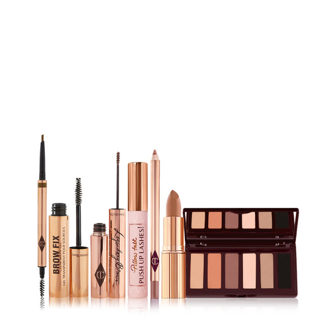 An open, double-ended eyebrow pen and brush, open eyebrow gel, and open eyebrow tint, all in gold-coloured tubes with a closed mascara in a nude pink tube with a gold-coloured lid, nude brown lip liner pencil, nude peach lipstick, and a 6-pan eyeshadow palette with a mirrored lid with matte eyeshadows in brown peach, and black shades. 