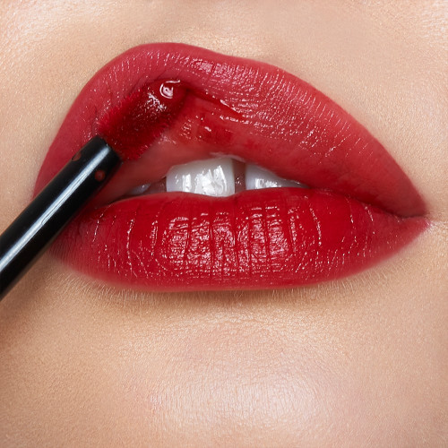 Lips close-up of a light-tone model applying a vibrant, poppy-red lip tint with a doe-foot brush applicator. 