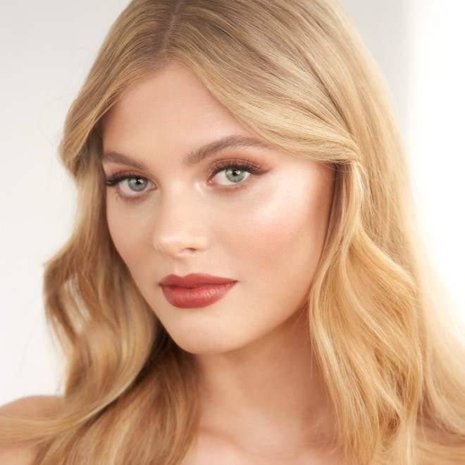 A fair-tone model with blue eyes wearing a matte lipstick in a golden peachy-pink shade. 