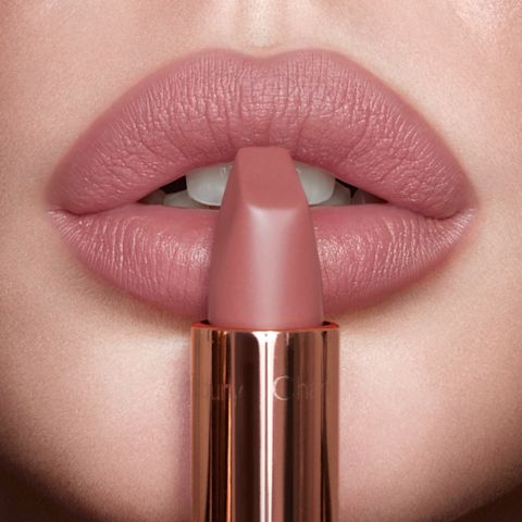 Lips close-up of a fair-tone model wearing a nude-pink matte lipstick while holding the lipstick in front of her lips.