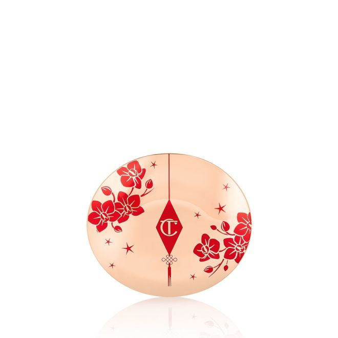 A closed powder compact with gold-coloured packaging and the CT logo printed on the lid in red and gold colour along with red cherry blossoms on the lid for the Lunar New Year.