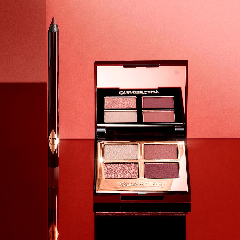 An open, mirrored-lid quad eyeshadow palette with berry-pink, red, rose gold, and beige eyeshadows and an eyeliner pencil in a dark copper shade. 