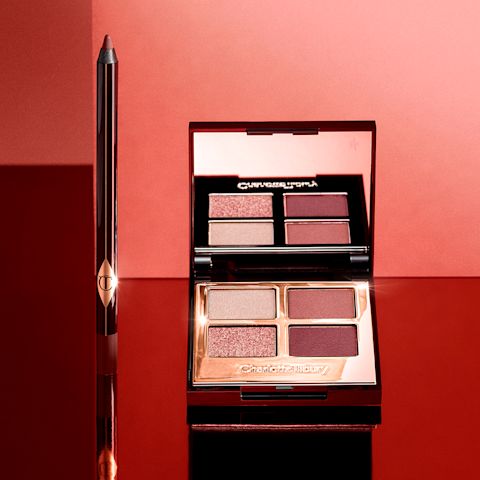 An open, mirrored-lid quad eyeshadow palette with berry-pink, red, rose gold, and beige eyeshadows and an eyeliner pencil in a dark copper shade. 