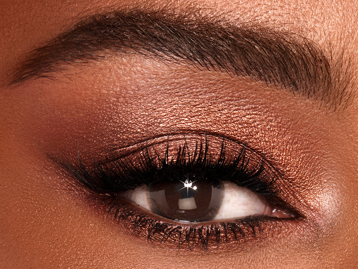 Single-eye close-up of a deep-tone model with brown eyes wearing shimmery brown and gold eyeshadow. 