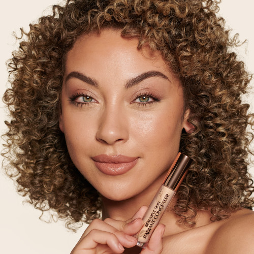 Medium-tone model with green eyes wearing a radiant, concealer that brightens, covers blemishes, and makes her skin look fresh along with nude lip gloss and subtle eye makeup.