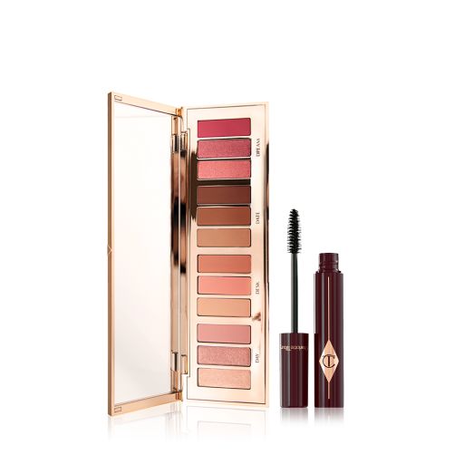 An opened, mirrored-lid eyeshadow palette containing eyeshadows in shades of peach, pink, champagne, and brown with by a mascara in a berry-brown bottle with its applicator next to it.   