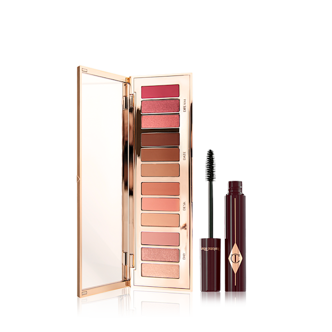 Pillow Talk Instant Eye Palette and Full Fat Lashes mascara An opened, mirrored-lid eyeshadow palette containing eyeshadows in shades of peach, pink, champagne, and brown with by a mascara in a berry-brown bottle with its applicator next to it.