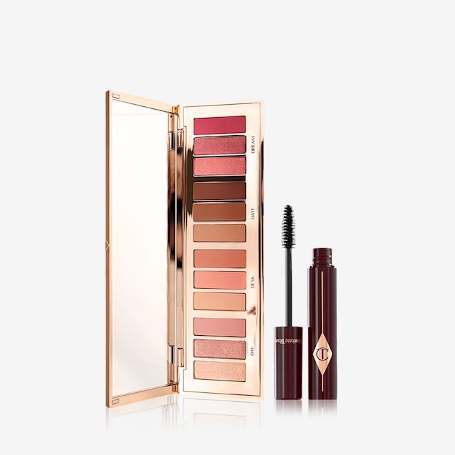 Pillow Talk Instant Eye Palette and Full Fat Lashes mascara An opened, mirrored-lid eyeshadow palette containing eyeshadows in shades of peach, pink, champagne, and brown with by a mascara in a berry-brown bottle with its applicator next to it.