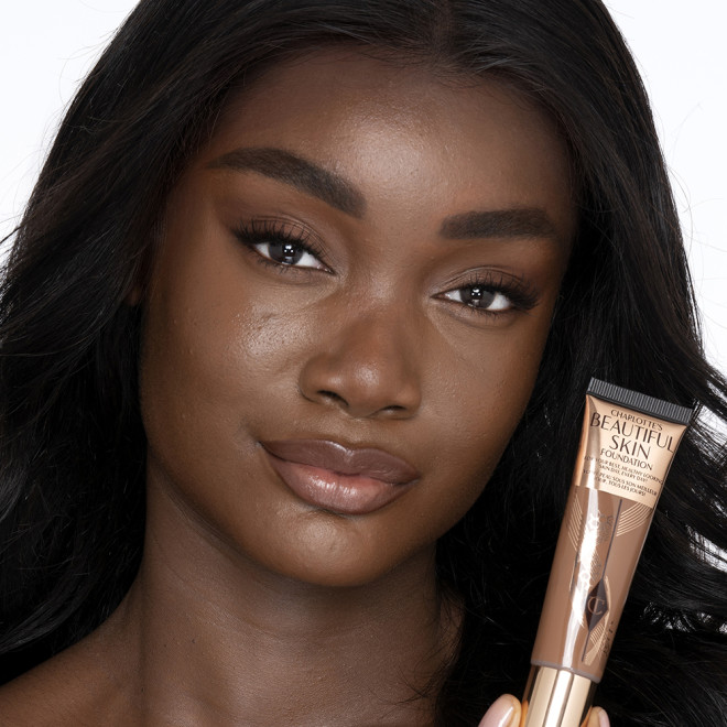 Deep-tone brunette model with brown eyes wearing nude pink lipstick with a skin-like foundation with a flawless, dewy finish. 