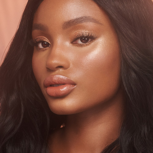 Deep-tone model wearing glowy, flawless face base with shimmery eye makeup, and a rosy terracotta coral lipstick with a satin-finish.