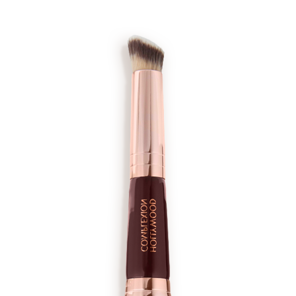 Close-up of a concealer brush with fawn and dark brown bristles with a rose-gold and dark crimson handle. 