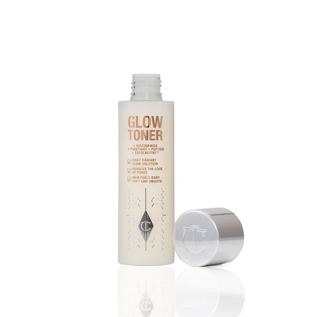 An open, large, clear bottle filled with luminous, cream-coloured watery toner with its silver-coloured lid next to it.