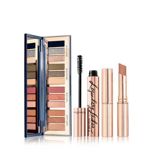 An open, mirrored-lid eyeshadow palette in twelve shimmery and matte eyeshadows in smokey grey, pink, and brown shades, an open mascara in golden packaging with its applicator next to it, and an open terracotta-brown, sparkly lipstick. 
