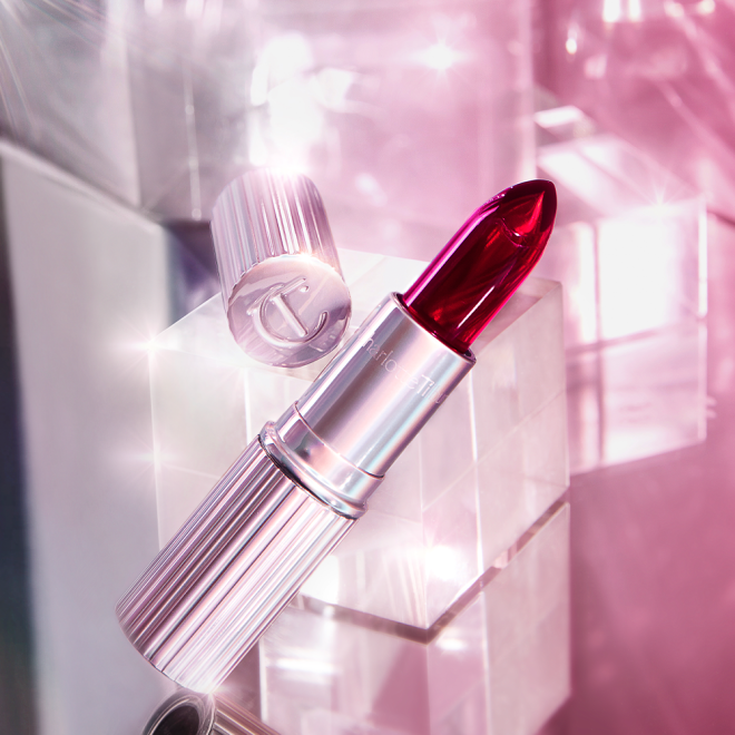 An open glowy, colour-changing lipstick in a sheer red colour with a luminous purple-coloured tube and lid. 