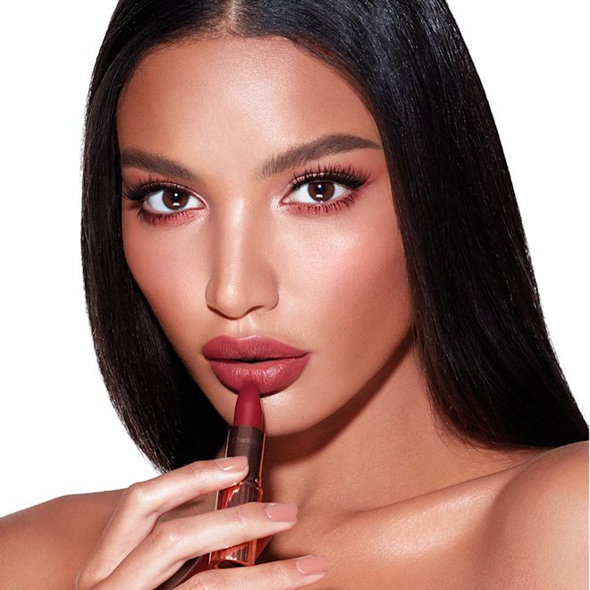 Matte Revolution in Walk of No Shame on medium-tone model Medium-tone model brunette model with brown eyes wearing warm pink blush with black eyeliner and applying dark berry-pink lipstick.