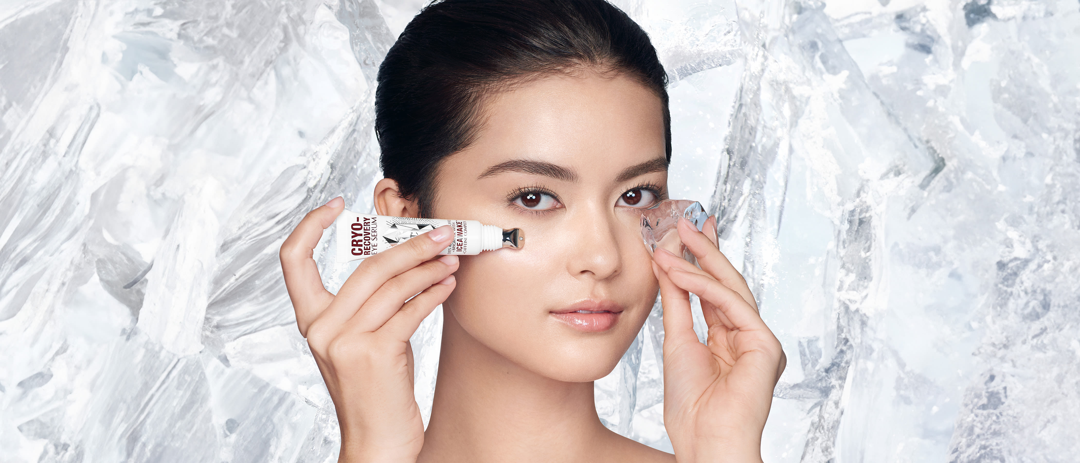 Model holding eye serum and ice to her under eye area