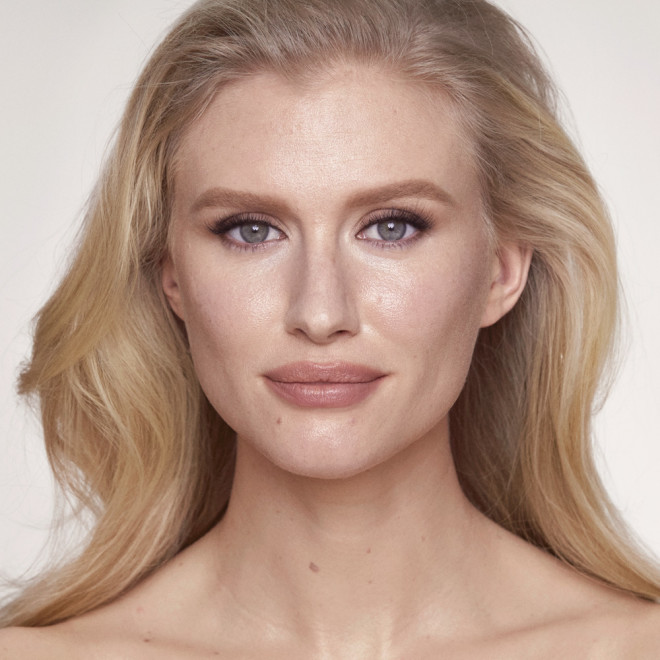 Fair-tone blonde model wearing glowy foundation in a cool-tone, light-beige shade that covers her pores and makes her skin look flawless and youthful.