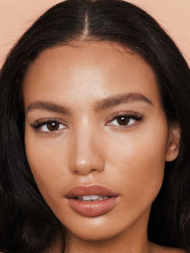 A medium-tone brunette model with a flawless face base, wearing natural-looking brown-toned makeup. 