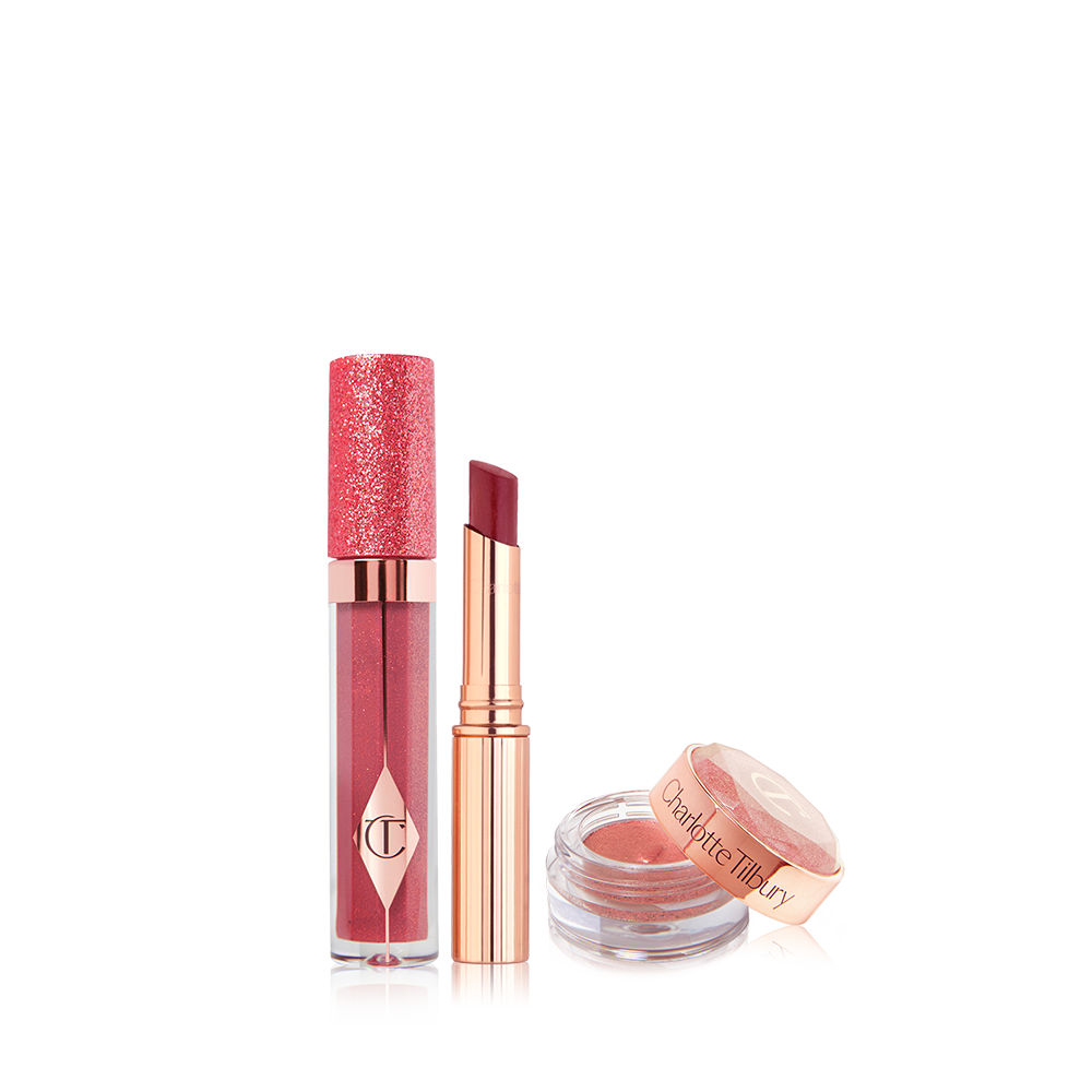 Glittery lip gloss in a berry pink shade in a glass tube with a glittery lid, sheer lipstick in a berry pink shade, and russet rose cream eyeshadow in a glass pot with its lid next to it.