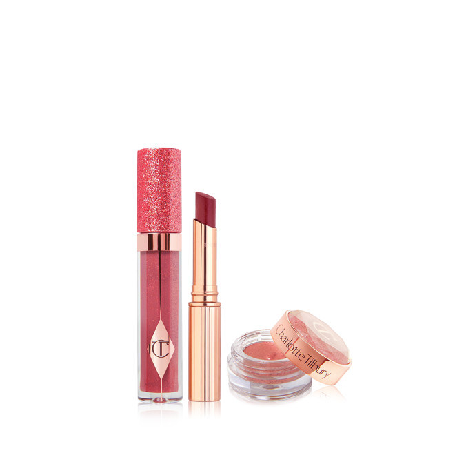 Glittery lip gloss in a berry pink shade in a glass tube with a glittery lid, sheer lipstick in a berry pink shade, and russet rose cream eyeshadow in a glass pot with its lid next to it.